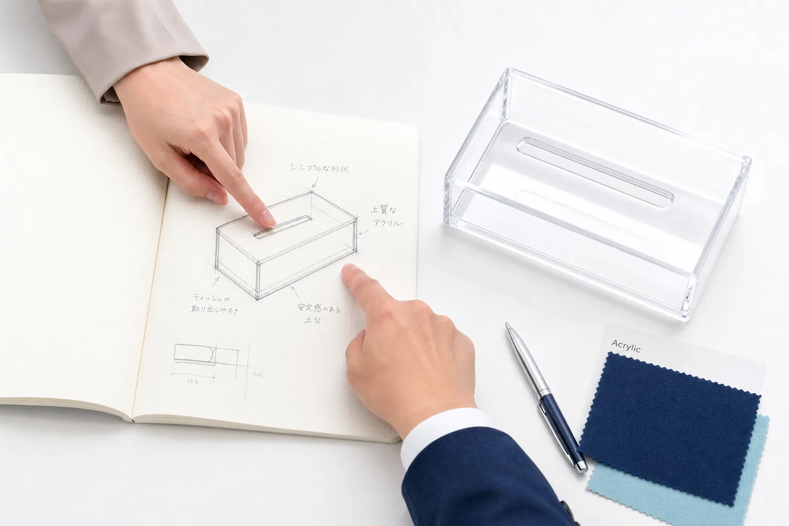 手描きのスケッチと完成した透明アクリル製品を指差しながらの打ち合わせ
